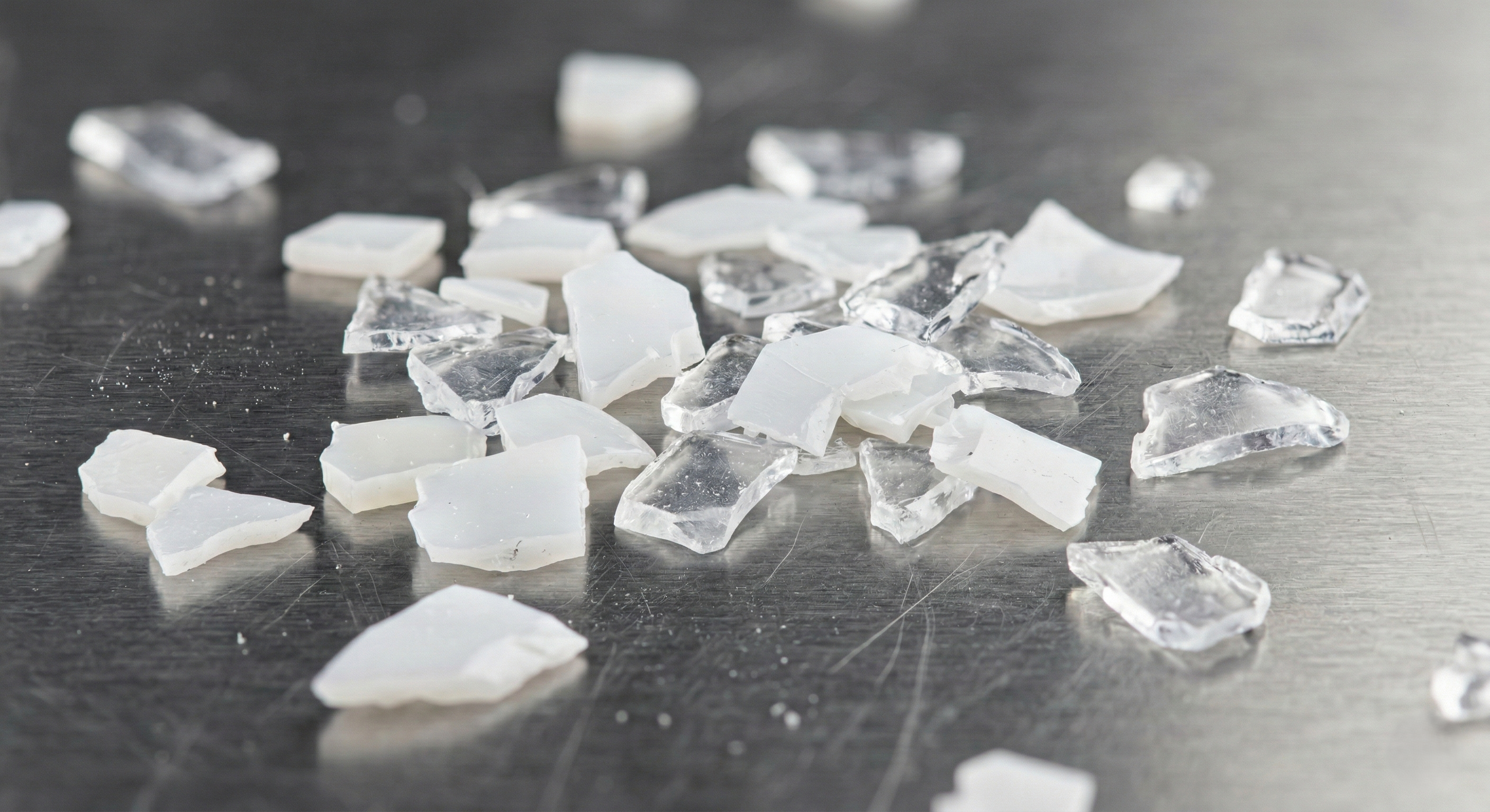 Macro photograph of clean white translucent plastic flakes on stainless steel surface